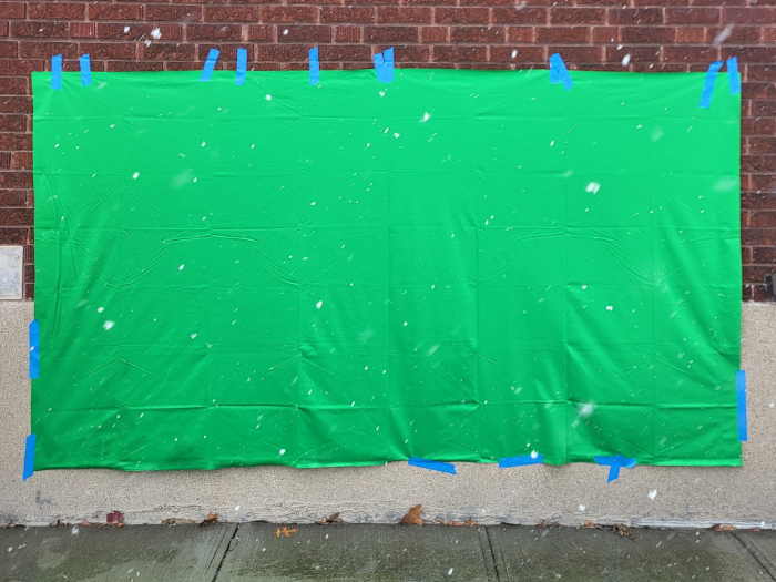 A green screen taped to a brick wall outside while snow falls