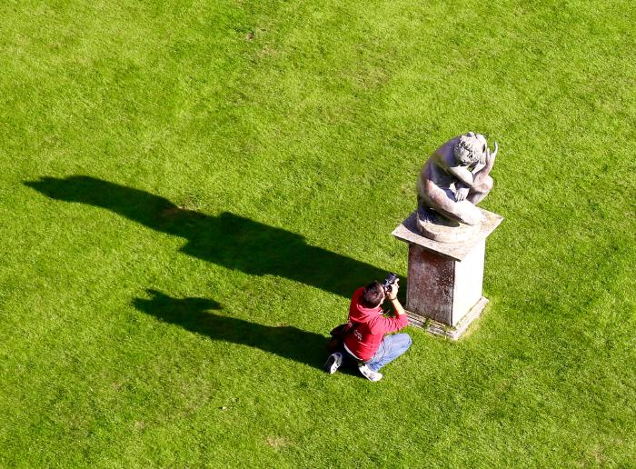 A photographer lowers himself to take a pictures of a very stoney model (because that model is a literal statue on a pedestal made of rock) [photo credit: Steve Hogan]